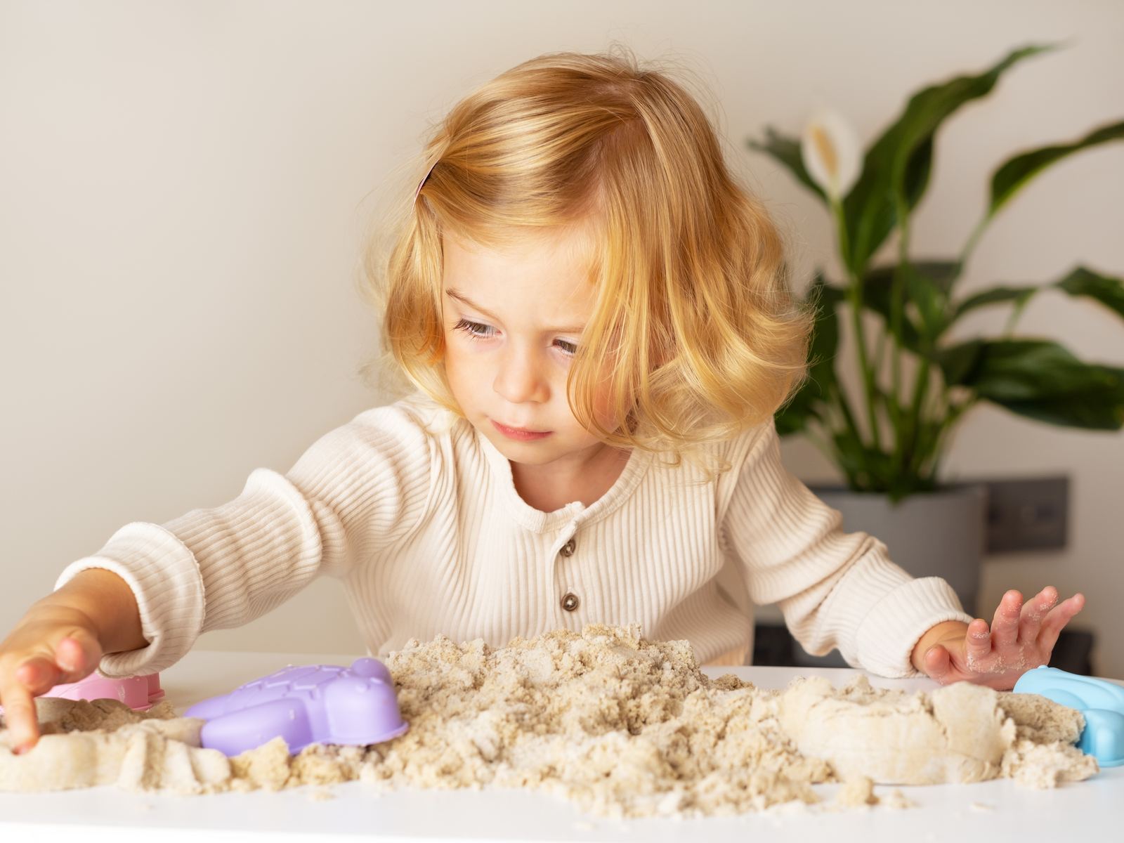 A young child absorbed in shaping kinetic sand with both hands at a table