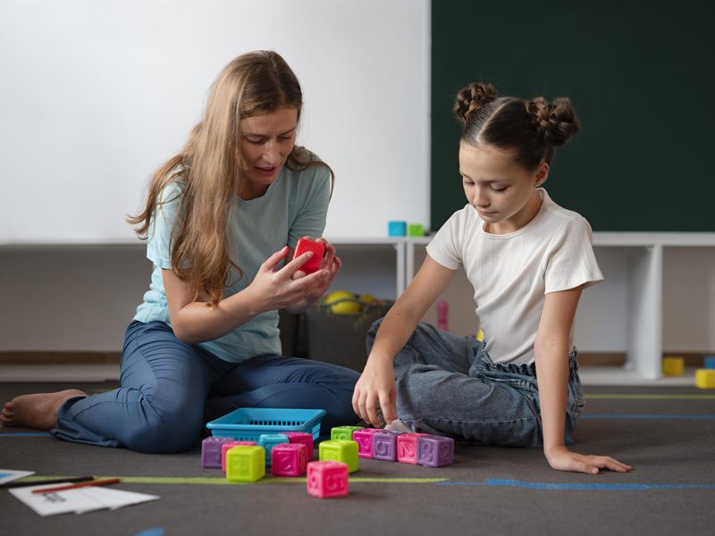 An adult and a child sitting on the floor building with coloured blocks