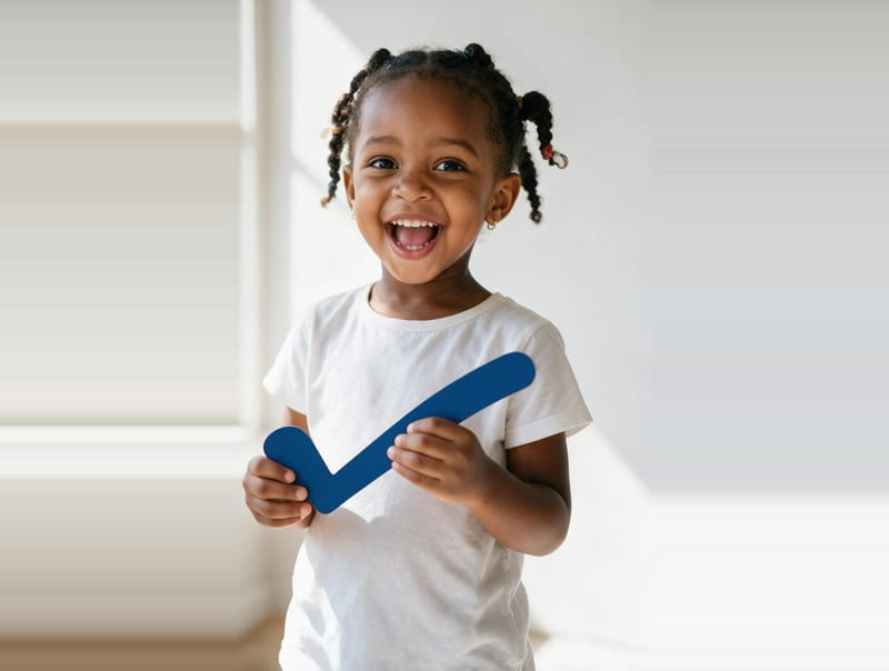 A laughing young girl in a white T-shirt holding up a large blue check mark